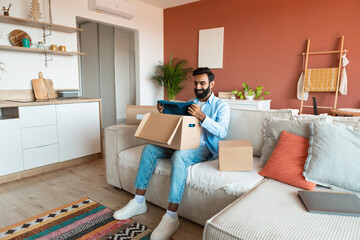 Middle Eastern guy holding new sweater unboxing delivered parcel indoors