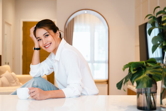 Smiling Woman Holding Coffee Cup Looking At Camera. Young Woman Drinking Tea Or Cofffee In Her Kitchen While Getting Ready To Go To Work.