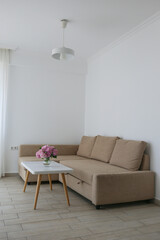 Spacious white room with beige corner sofa and a bouquet of hortensia flowers on a marble table....
