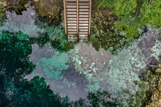 Aerial view of Madison Blue Spring State Park with stairs going down into the clear blue water with rocks and vegetation around in the town of Lee, Florida, United States.