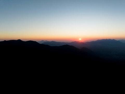 Aerial view of the sun setting down across the valley in Serino along the Mount Terminio National park revealing the Mount Vesuvio in distance, Campania, Avellino, Italy.