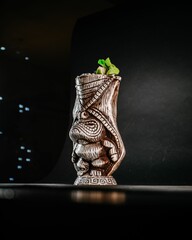 Cocktail inside a wooden carved tropical cup on a dark surface