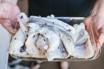 a female holding raw marinated fish in a glass tray