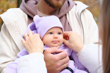 Young mother and father are walking with a newborn baby in the autumn park. The mother straightens the cap to the child, the child looks at the mother. Close-up