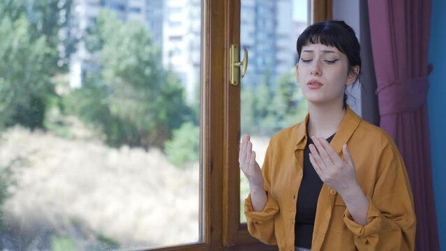 Muslim young woman praying in front of the window.