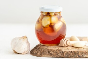 Jar of honey with garlic inside and a honeycomb, on a white background, home remedy for flu