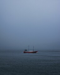a red boat floating across the blue water in foggy day