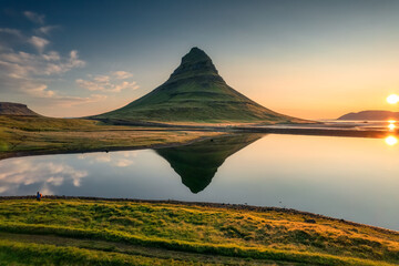 Volcanic Kirkjufell mountain with lake reflection and traveler man standing during sunrise at Iceland