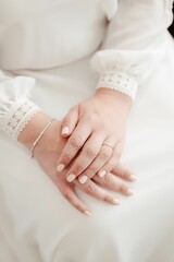 Young woman in wedding dress, sitting with her hands folded on her knees wearing an engagement ring