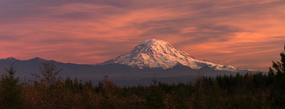 Scenic view of Mount Rainier illuminated by a vibrant pink sky at sunset.
