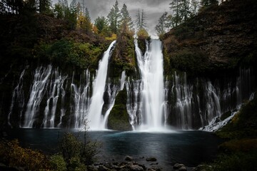 Fototapeta premium a waterfall is seen next to some trees on a hillside
