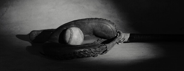 Old used baseball in vintage leather ball glove for sports nostalgia background in black and white.