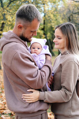Young mother and father are walking with a newborn baby in the autumn park. Parents look at the child with tenderness