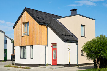 Two storey cottage or bungalow with closed red door standing in front of camera against blue sky in non-urban environment