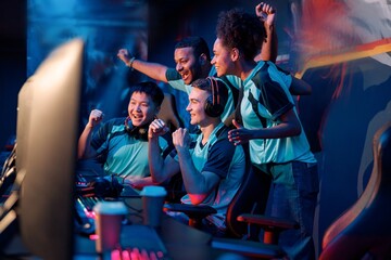 Multiracial cybersport gamers expressing success while raising hands up and smiling during participation in esports tournament in computer club