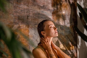 Portrait of young woman standing with eyes closed and washing her body while taking shower. Spa, beauty and care concept
