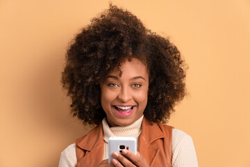 joyful afro brazilian woman watching video and photos on mobile smartphone in beige background. communication, app, connection concept.