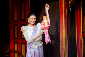 Young Asian woman with contemporary Thai dress stand and hold pink traditional lantern in area of ancient building and she look happy. © narong