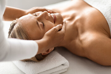 Fototapeta na wymiar Closeup Of Smiling Middle Aged Female Having Face Massage In Spa Salon