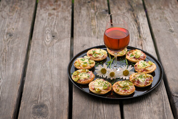 a small snack, pizzas piccolo on black plate with a glass of wine, on a wood table