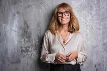 Portrait of a confident mid aged woman looking at camera and cheerful smiling against grey wall