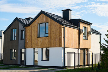 Two small cottages of pastel colors standing next to one another in rural environment against cloudy sky on summer day