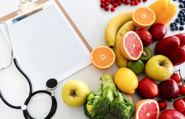 Stethoscope, paper on tablet with empty space, fruits, berries and vegetables