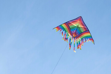 Kite in a blue sky. Rainbow Delta Kite flying among the clouds. Happy growing years moment. Outdoor time spending. Aspirations, target, inspiration concept. Freedom and summer holiday. Childhood dream