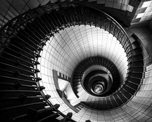 Grayscale high angle shot of a curving spiral staircase in a building