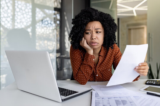 Sad disappointed businesswoman inside office at workplace looking at documents papers financial reports, african american female worker on paper work depressed unhappy with financial achievements