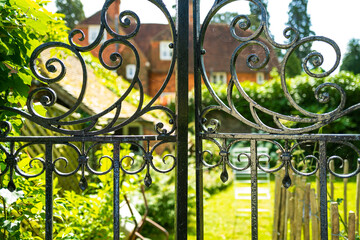 Fototapeta na wymiar Shallow focus of an ornate wrought iron gate leading to a private garden. A large house can be seen in the distance.