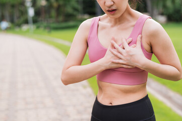 Woman jogger. young asian female wearing pink sportswear holding hands on chest after running in public park. Healthcare exercise pain concept.