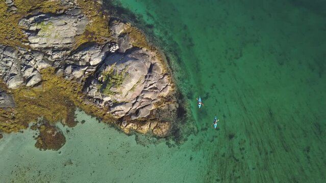 Two kayakers paddling an inflatable kayak on a Norwegian fjord, rocky archipelago, white sandy beach, turquoise sea, aerial view with camera drone, Gimsoy, Lofoten, Nordland, Norway, Europe