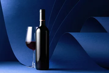 Gordijnen Bottle and glass of red wine on a blue background. © Igor Normann