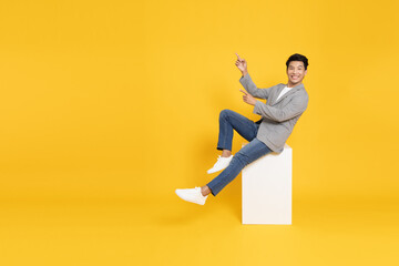 Fototapeta na wymiar Young Asian businessman sitting and pointing to empty copy space isolated on yellow background