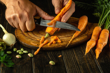 The cook cleans fresh carrots on the kitchen table before adding them to vegetable borscht....