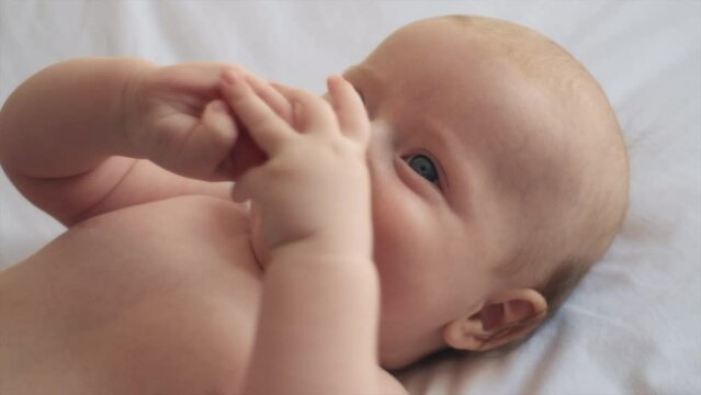 Close up portrait of cheerful cute newborn baby lying down alone on comfy white bed at home. Adorable smiling infant boy rests on cozy bedsheets, Infancy, healthcare and paediatrics, babyhood concept