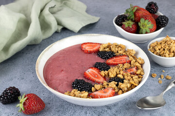 Smoothie bowl with strawberries, blackberries and granola on a blue background. Healthy breakfast. Vegan food concept.