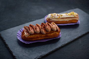 Two delicious eclair cakes - tiramisu and pistachio flavoured covered with cream, icing and chopped...