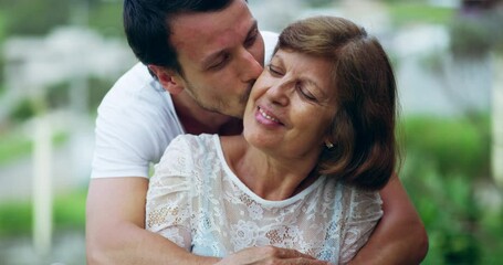 Senior woman, hugging and adult child kissing his mother on the cheek with love, care and happiness in a park. Happy, smile and male person embracing his mature mom in retirement in an outdoor garden