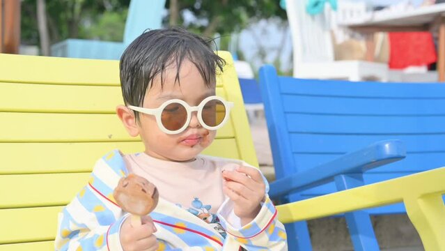 Asian boy sitting on a beach chair eating ice cream.