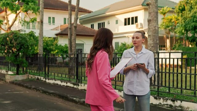 In a posh residential area, a realtor and her client are sharing a laugh while standing in front of houses