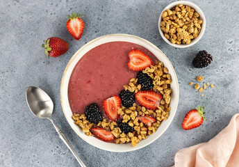 Smoothie bowl with strawberries, blackberries and granola on a blue background. Healthy breakfast. Top view.