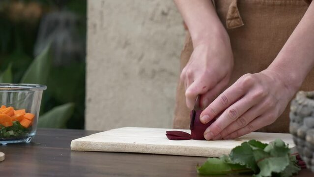 Woman in brown clothes cooking vegetable salad, cut beet with knife on board, Wroclaw, Poland