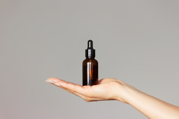 a dark glass bottle with a dropper lid is held in a woman's hand on a light background. Skin care....