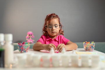 Obraz na płótnie Canvas A beautiful little girl with crimson hair, wearing a pink shirt and safety glasses is playing educational games at the table