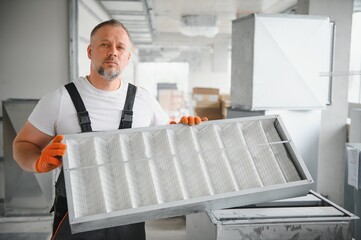 A male worker holds an air filter for air conditioning in an office space. Installation of an air conditioner.