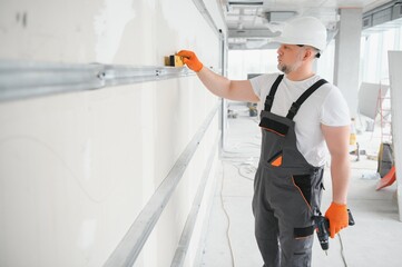 Man holding level against plasterboard, interior drywall. Attic renovation - obrazy, fototapety, plakaty