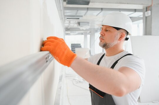 man drywall worker or plasterer putting mesh tape for plasterboard on a wall using a spatula and plaster. Wearing white hardhat, work gloves and safety glasses. Image with copy space.