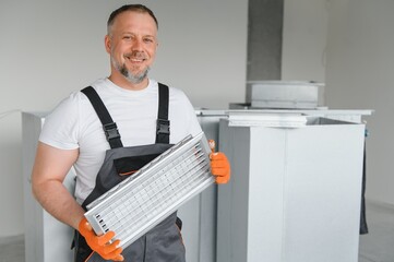 A male worker holds an air filter for air conditioning in an office space. Installation of an air...